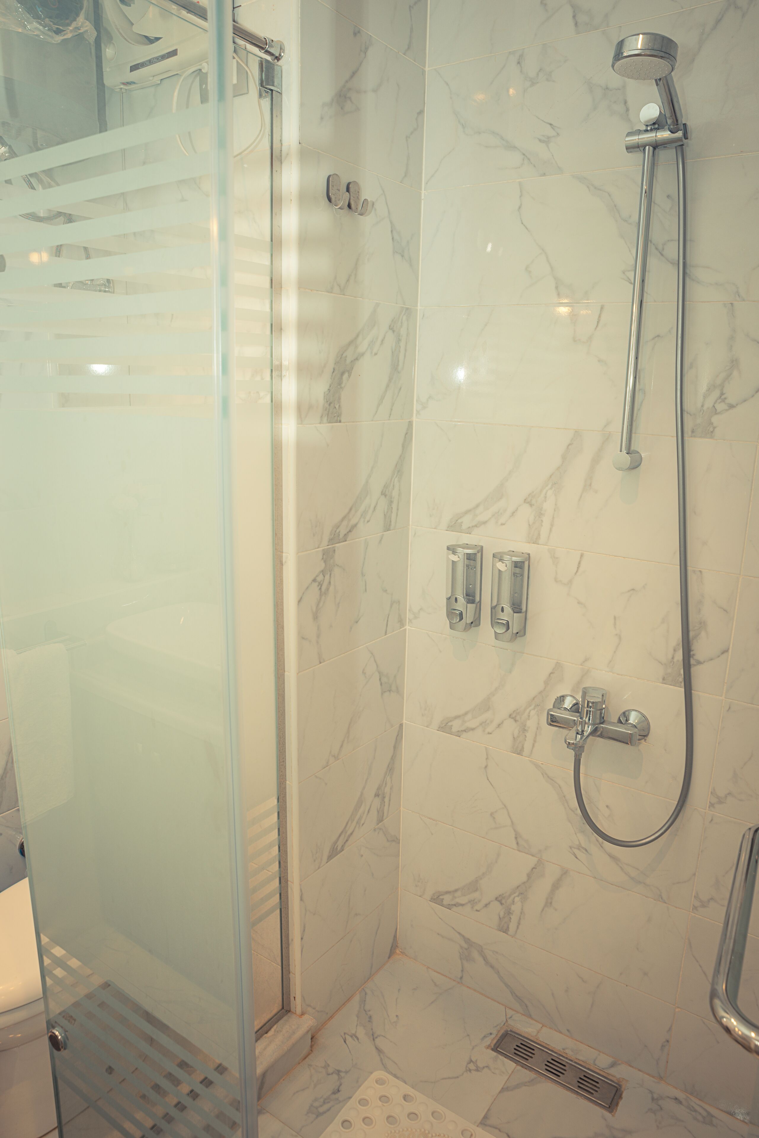 A glass-enclosed shower with a handheld showerhead and a wall-mounted faucet.