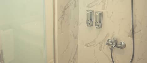 A glass-enclosed shower with a handheld showerhead and a wall-mounted faucet.