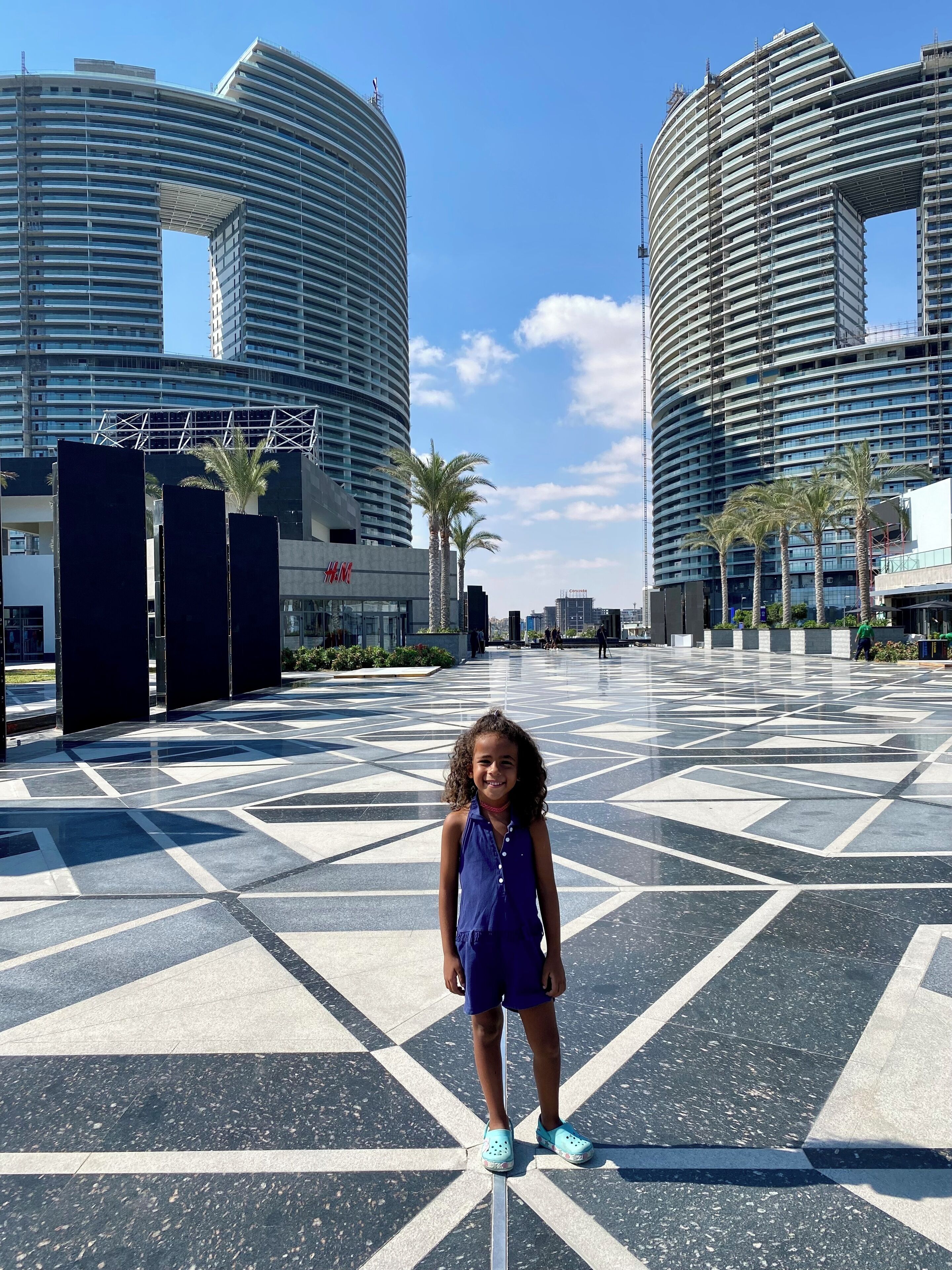 Un niño parado en una plaza rodeada de edificios modernos y palmeras.