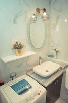 Un baño moderno con pared de mármol, un lavamanos independiente, una lavadora y un estante con una planta en maceta.
