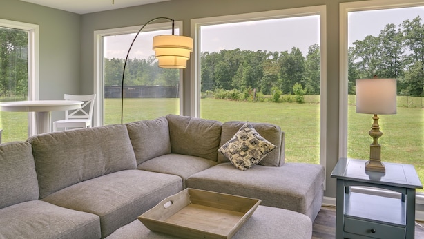 A sectional sofa with a cushion, a wooden tray, a lamp, and a view of a grassy yard through large windows. - Tullahoma Vacation Rental < 8 Mi to Lynchburg! (Tullahoma)