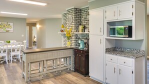 A modern kitchen with white cabinetry, a black brick accent wall, a built-in microwave, and a dining area with white chairs and a wooden table. - Tullahoma Vacation Rental < 8 Mi to Lynchburg! (Tullahoma)