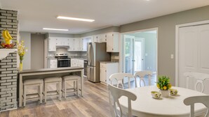 A modern kitchen with white cabinets, a central island, and a dining area with white chairs. - Tullahoma Vacation Rental < 8 Mi to Lynchburg! (Tullahoma)