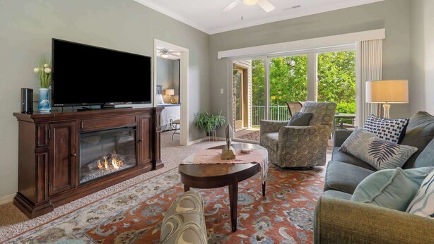 Una sala de estar con chimenea, televisor, ventilador de techo y vistas al exterior.