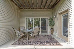 Relax on the covered patio with a table and four chairs, surrounded by a decorative rug and a potted plant.