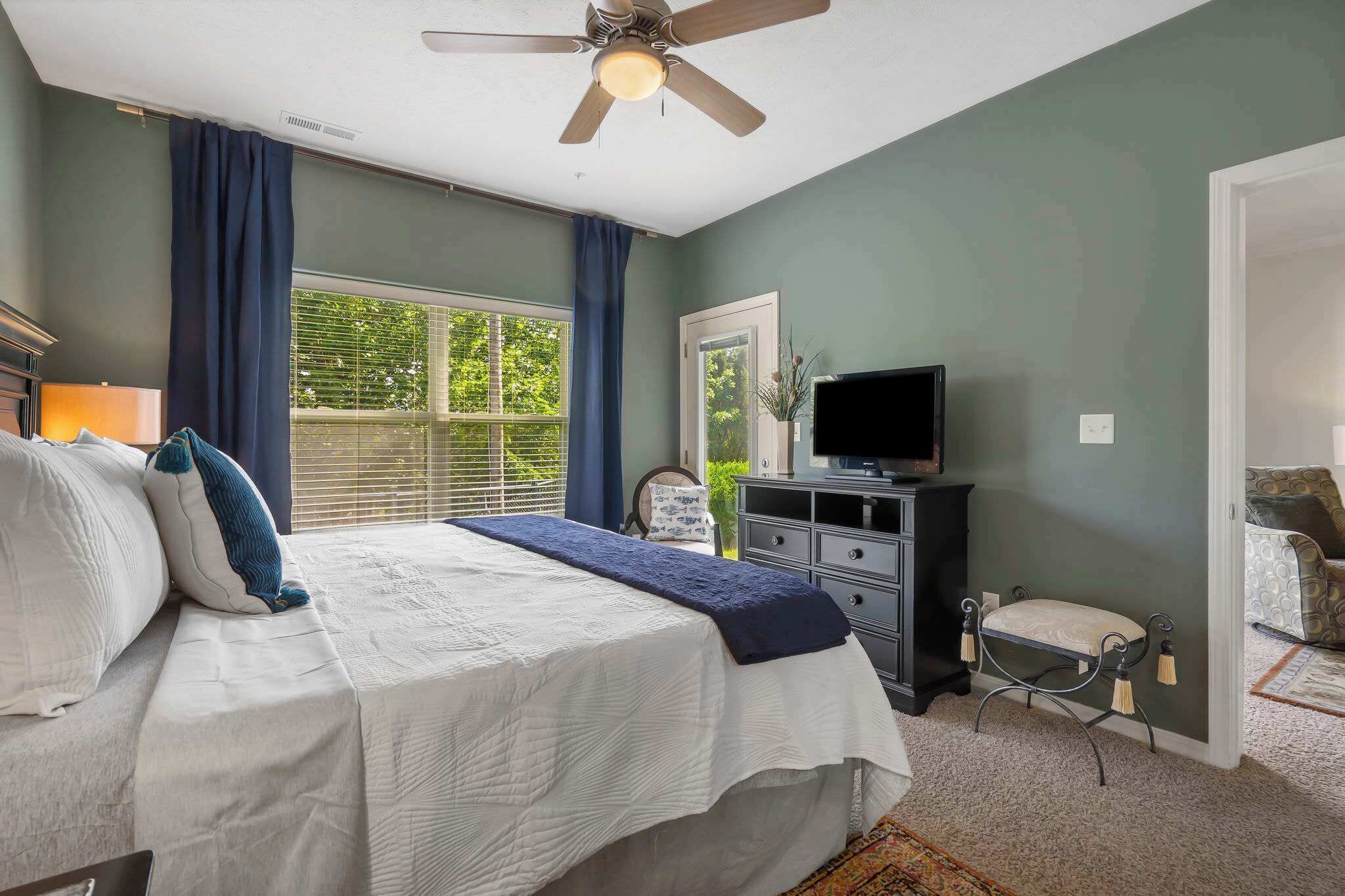 Un dormitorio con cama, cómoda, televisor y ventana con cortinas.