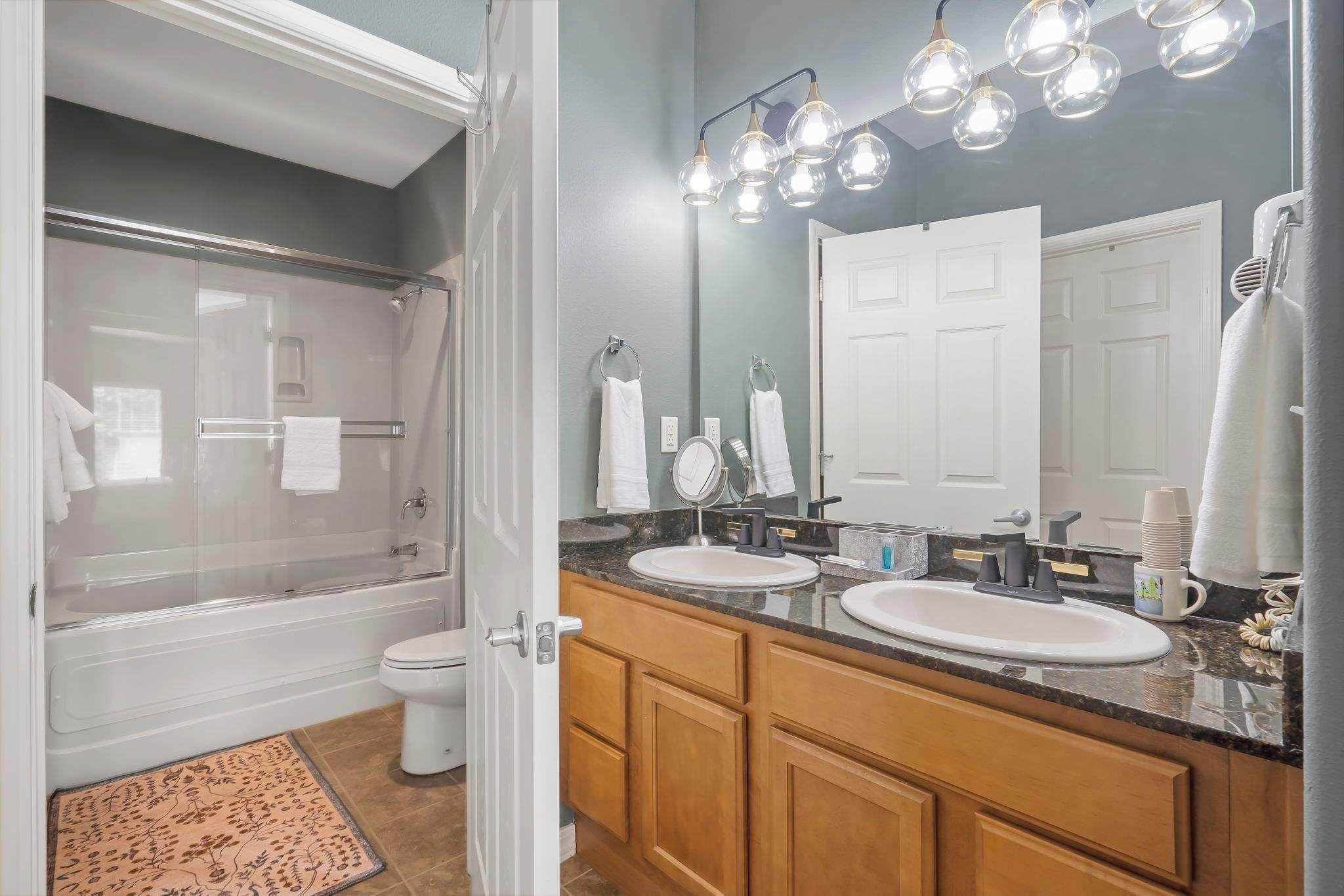 A bathroom with a glass-enclosed shower, two sinks, a large mirror, and a towel rack.