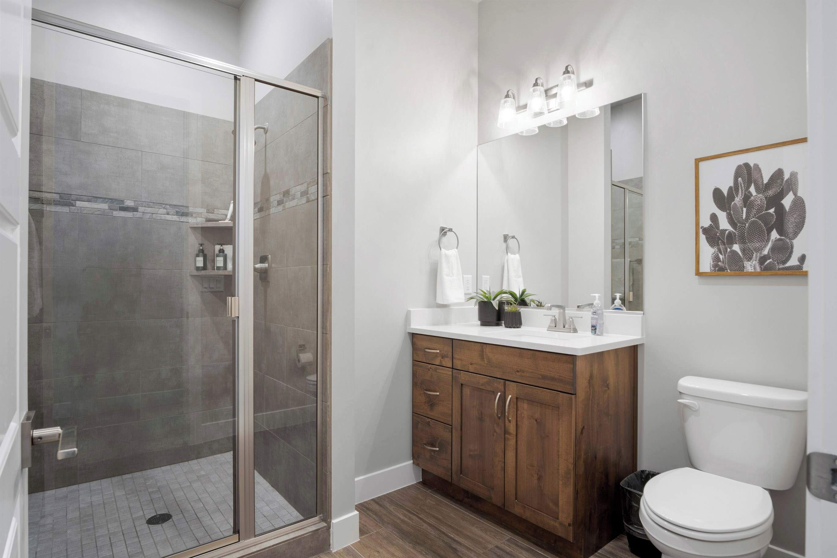 A modern bathroom with a glass-enclosed shower, wooden vanity, and a large mirror.
