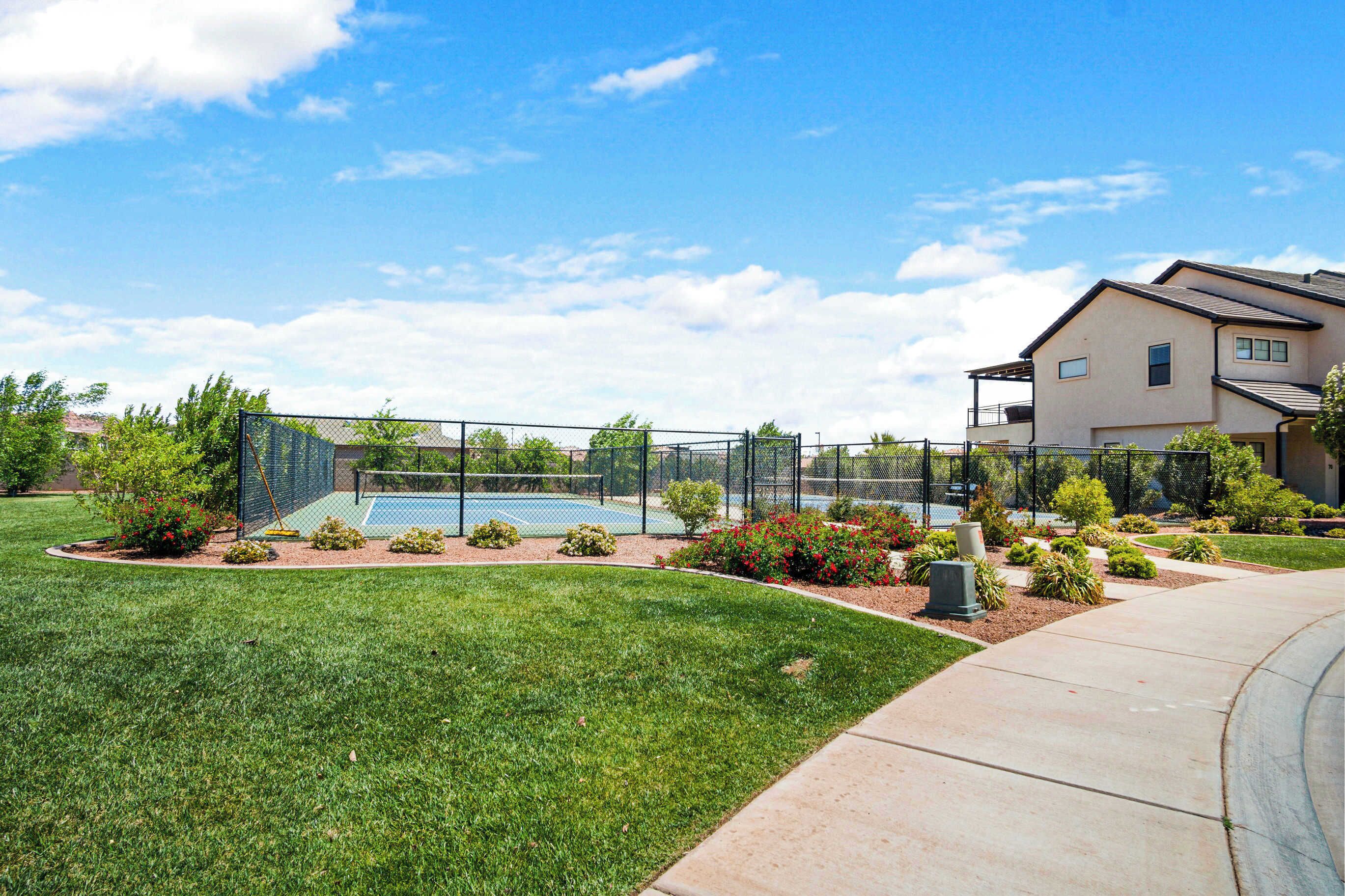 A residential area with a tennis court, well-maintained lawn, and a house with a balcony.