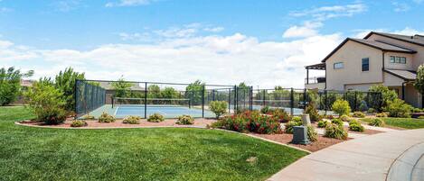 Un quartier résidentiel doté d’un court de tennis, d’une pelouse bien entretenue et d’une maison avec balcon.