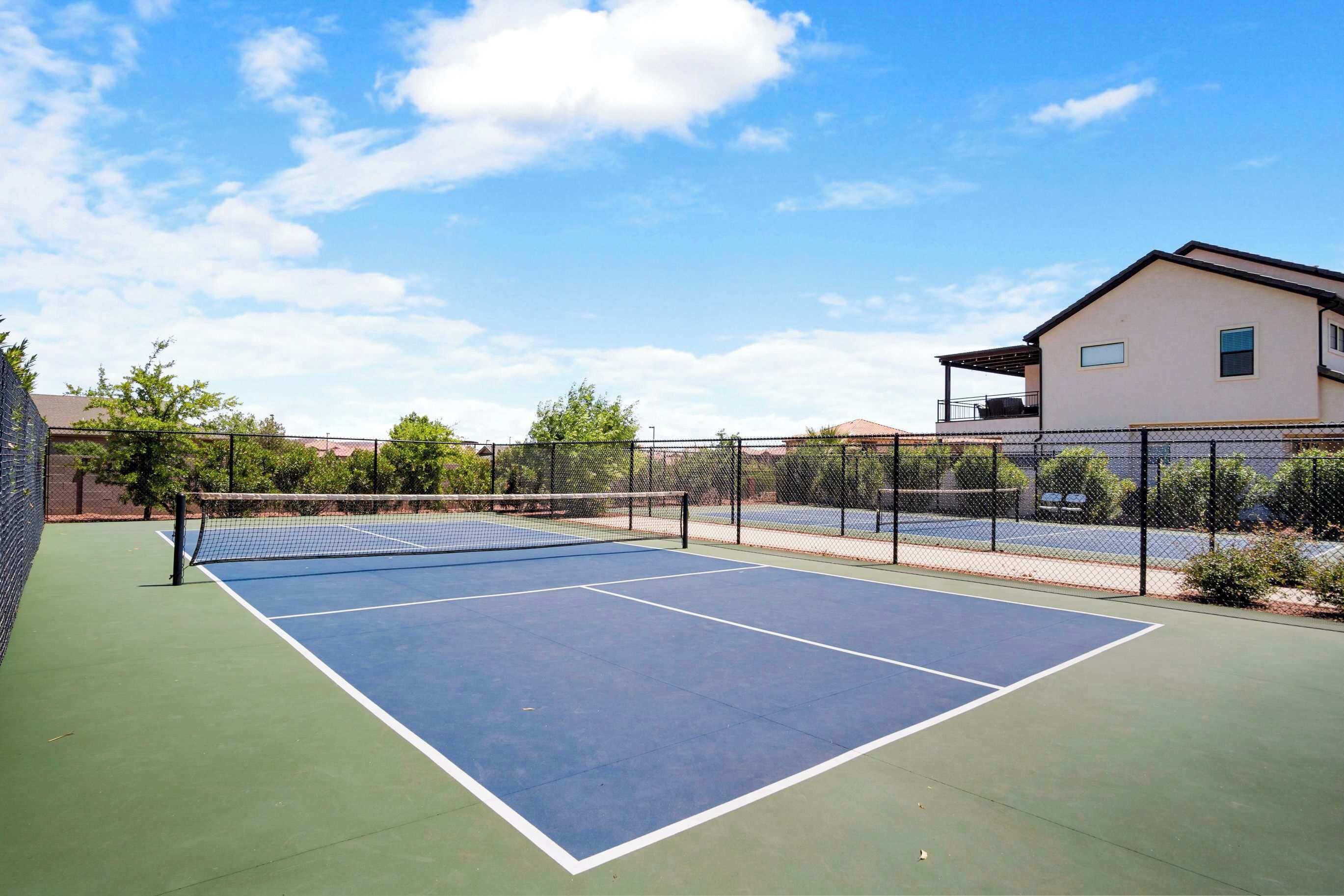 An outdoor tennis court with a net, surrounded by a fence and trees.