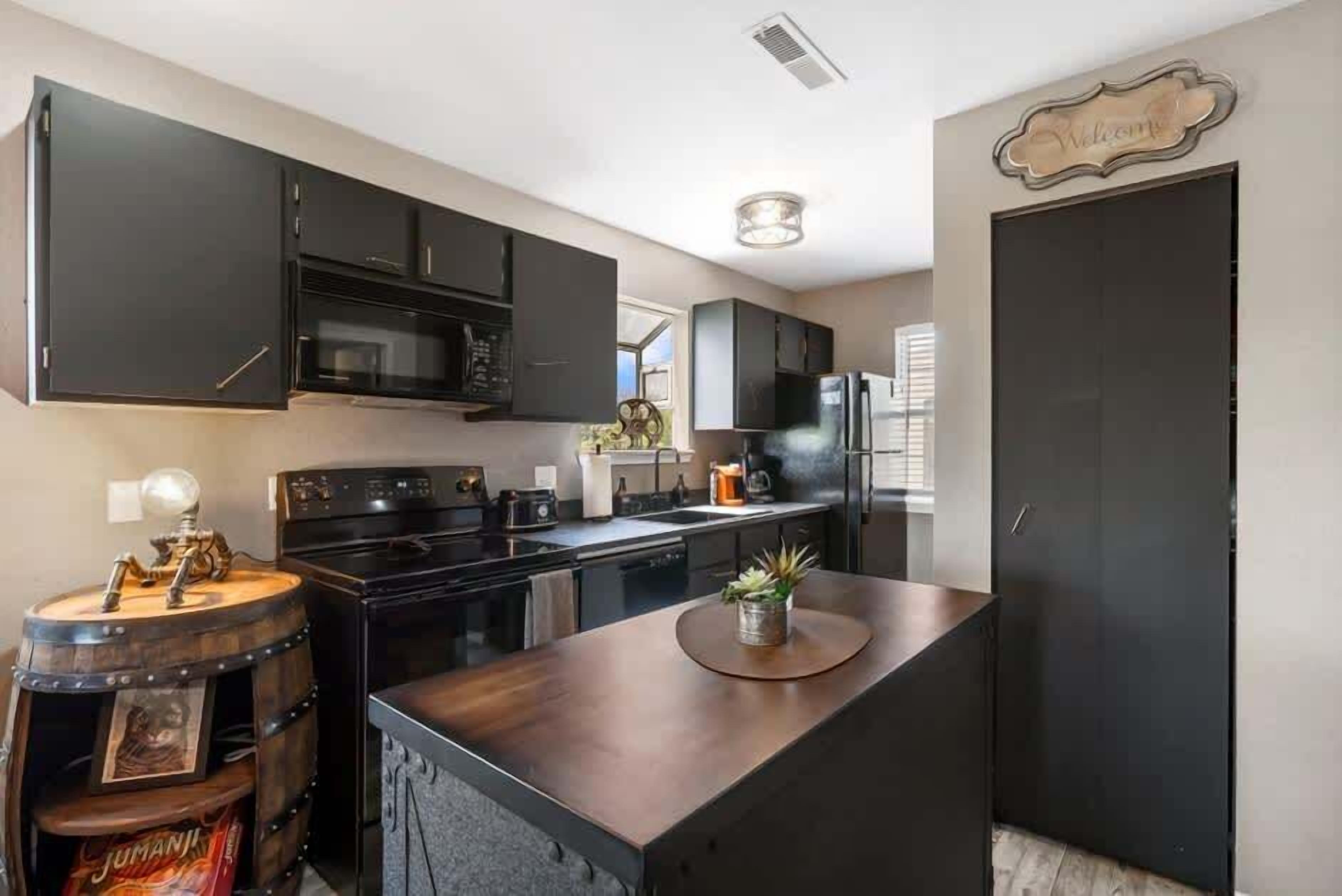 Una cocina moderna con armarios oscuros, una isla central y un letrero de bienvenida.