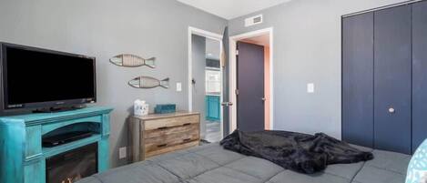 A bedroom with a bed, a TV, a ceiling fan, and a door leading to another room.