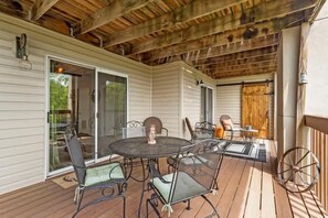 En overdækket terrasse med et rundt bord og stole, en træterrasse og en skydedør, der fører til en baghave.