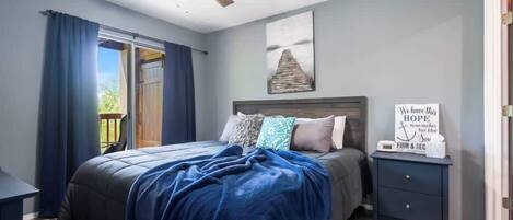A bedroom with a bed, a ceiling fan, a nightstand with a sign, and a window with curtains.