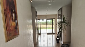 Un couloir avec un sol carrelé, un tableau encadré sur le côté gauche et une plante en pot sur le côté droit.