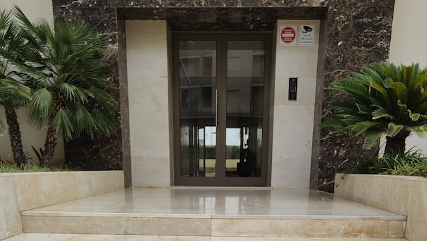 Un escalier en marbre menant à l’entrée d’un bâtiment, avec une porte en verre et un panneau indiquant qu’il est interdit de fumer.