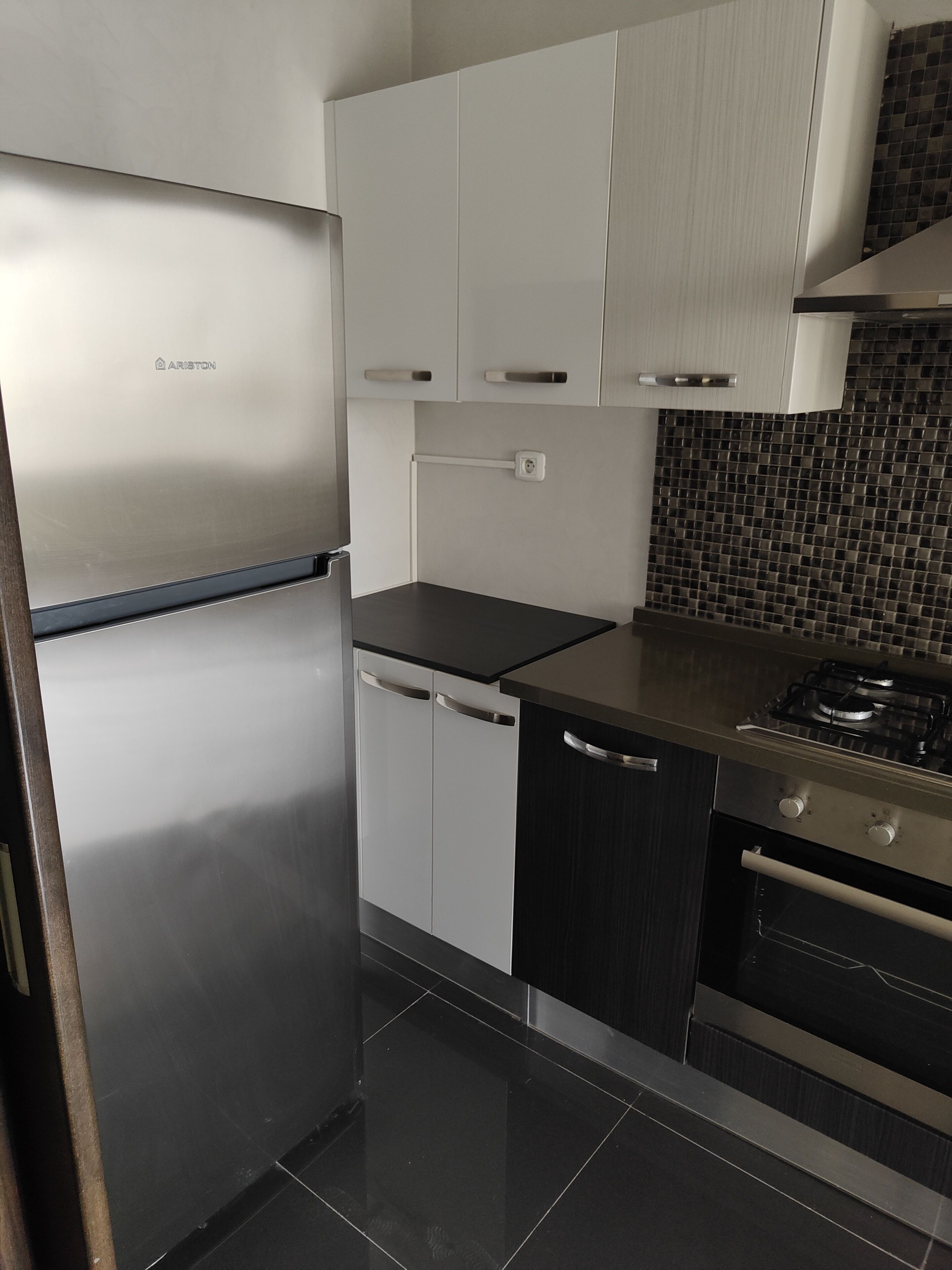 Una cocina moderna con electrodomésticos de acero inoxidable, armarios blancos y un salpicadero de azulejos negros.
