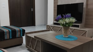 Un salon moderne avec une table basse en bois, un canapé, un téléviseur fixé au mur et une porte visible au fond.