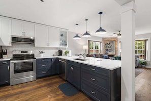A modern kitchen with white cabinets, stainless steel appliances, dark blue cabinetry, and pendant lighting.