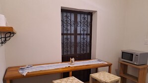 Une petite cuisine avec une table en bois, quatre tabourets en osier, un four à micro-ondes posé sur une étagère et une porte en métal décorative.
