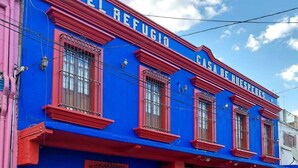 Un bâtiment à la façade bleue et aux détails rouges, doté de nombreuses fenêtres et d’une entrée fermée par un portail.