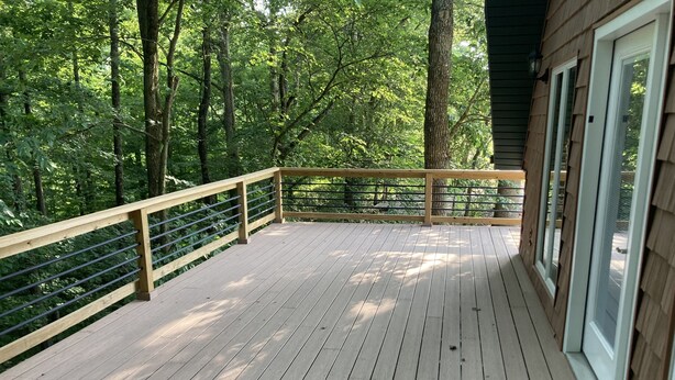 Eine Holzterrasse mit Metallgeländer, umgeben von Bäumen.