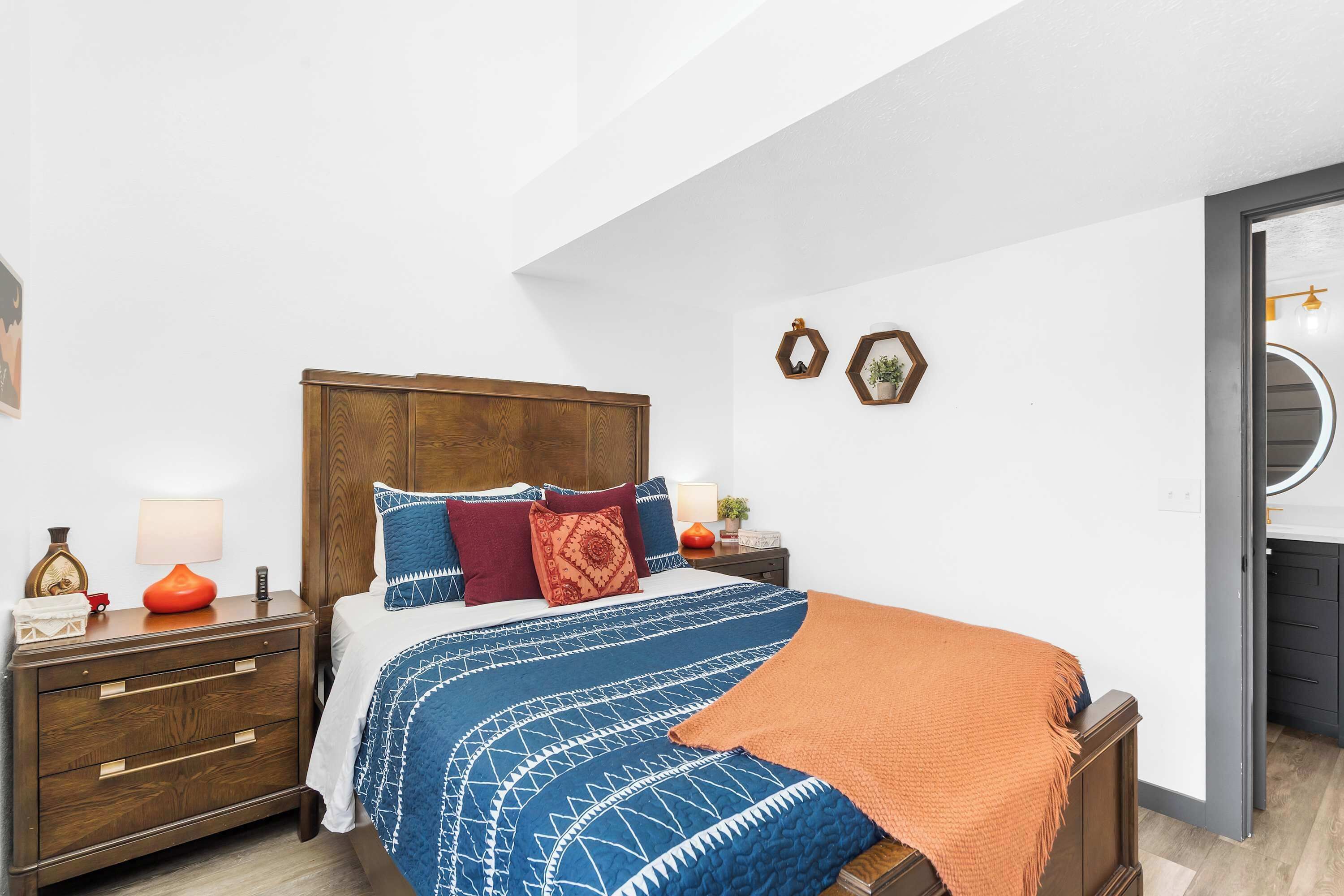 A bedroom with a wooden bed, a nightstand, a lamp, and a small table with decorative items.