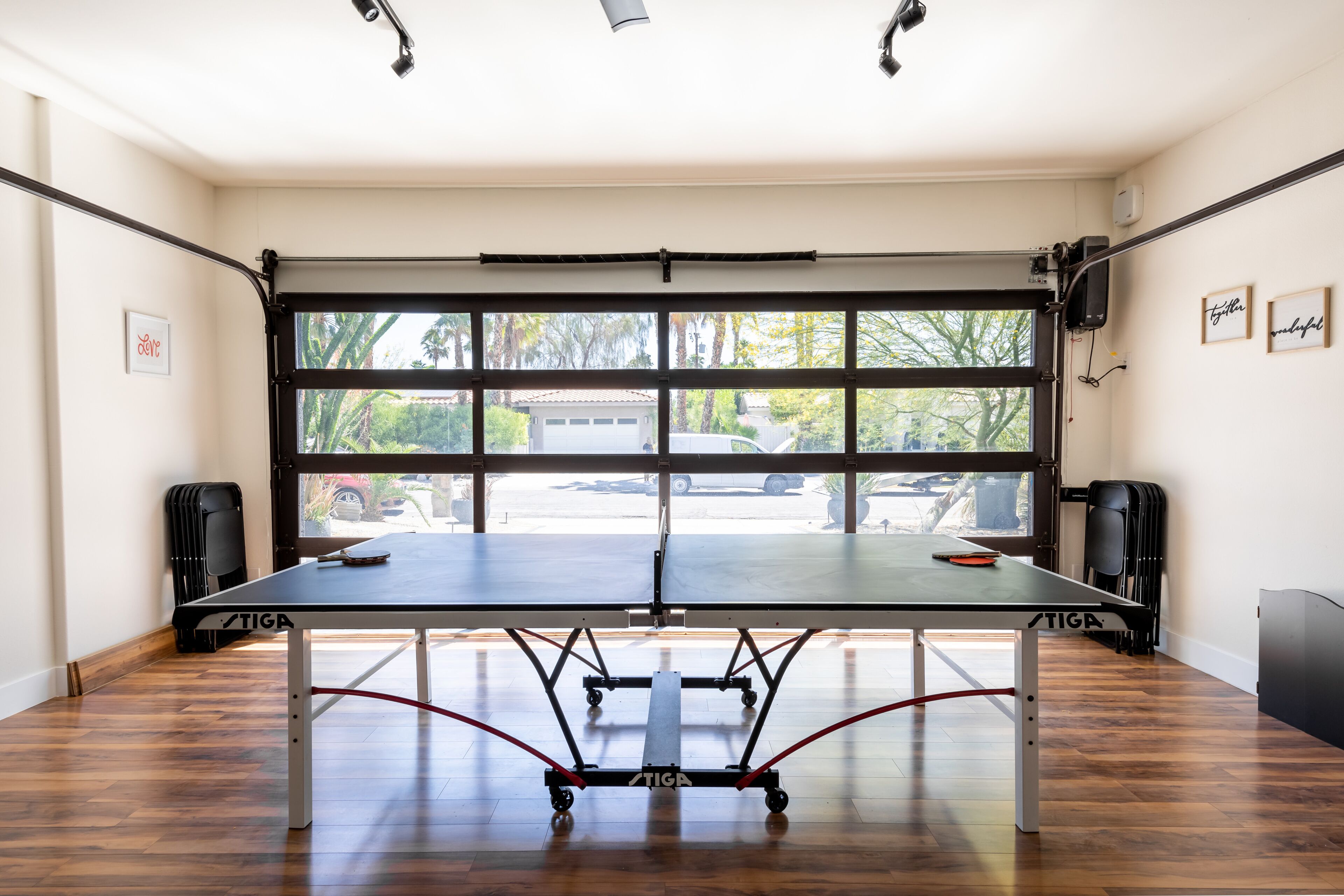 Una mesa de ping pong en una habitación con ventanas amplias, suelo de madera y dos altavoces.