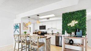 A modern kitchen with white cabinets, a wooden island, and a green wall with a 'coffee' sign. - SnowBirdsWelcome-GulfView-HeatedPool (Destin)
