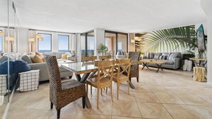 A spacious living area with a glass dining table, comfortable seating, and a large window offering a view of the ocean. - SnowBirdsWelcome-GulfView-HeatedPool (Destin)