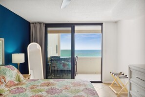 A bedroom with a bed, a nightstand, a lamp, a chair, a table, and a view of the ocean through a sliding door. - SnowBirdsWelcome-GulfView-HeatedPool (Destin)