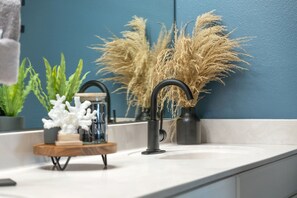 A modern bathroom with a white sink, a black faucet, and decorative plants including pampas grass. - SnowBirdsWelcome-GulfView-HeatedPool (Destin)