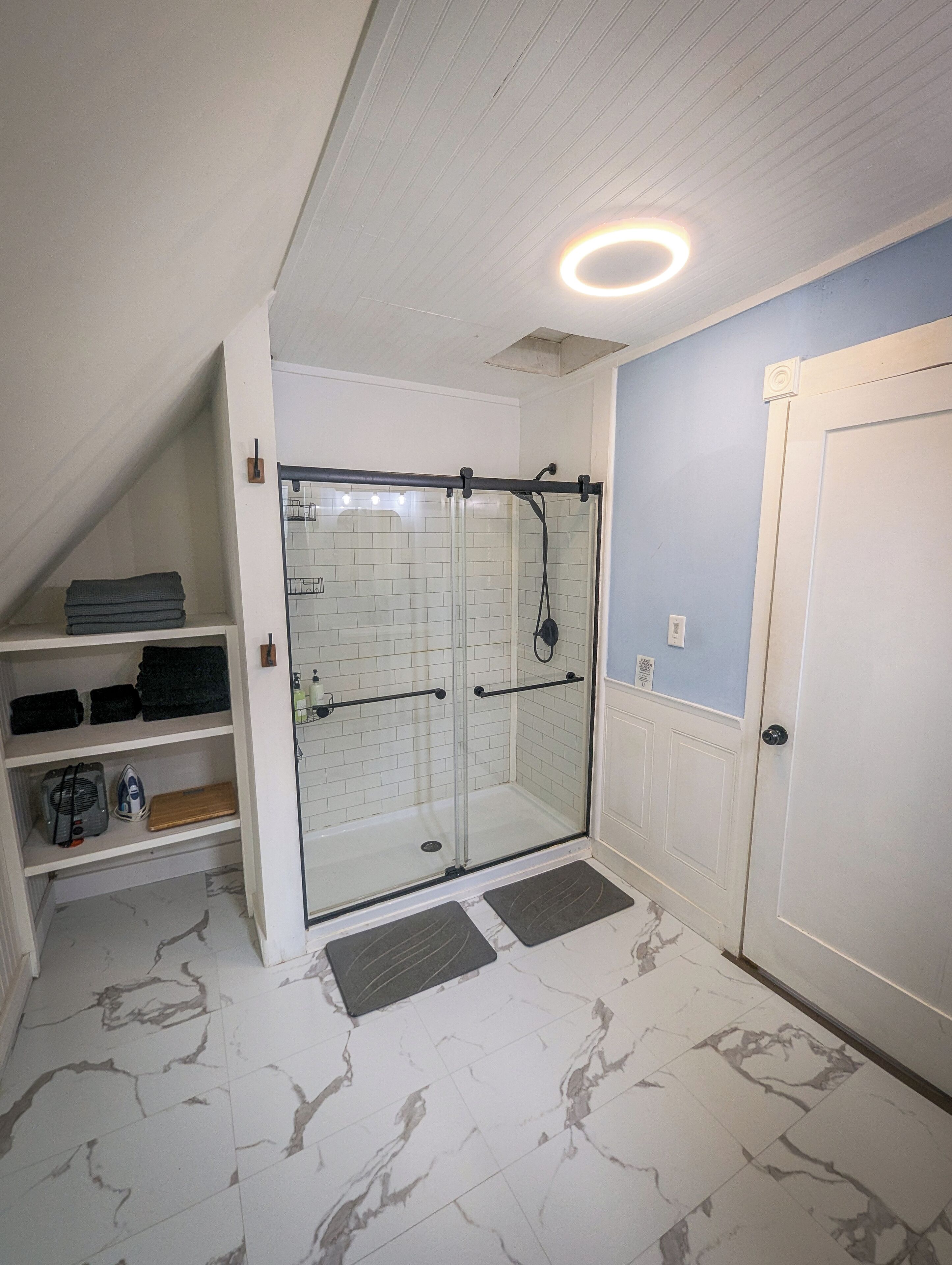 Un baño moderno con cabina de ducha de vidrio, paredes con azulejos blancos y suelo de mármol.
