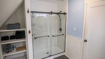 Un baño moderno con cabina de ducha de vidrio, paredes con azulejos blancos y suelo de mármol.