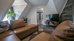 Un salon moderne de style loft, avec un canapé en cuir marron, un téléviseur à écran plat et un mur décoratif en bois.