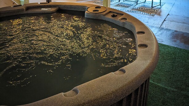 Un bain à remous entouré de pierres, avec des poutres en bois et des guirlandes lumineuses.