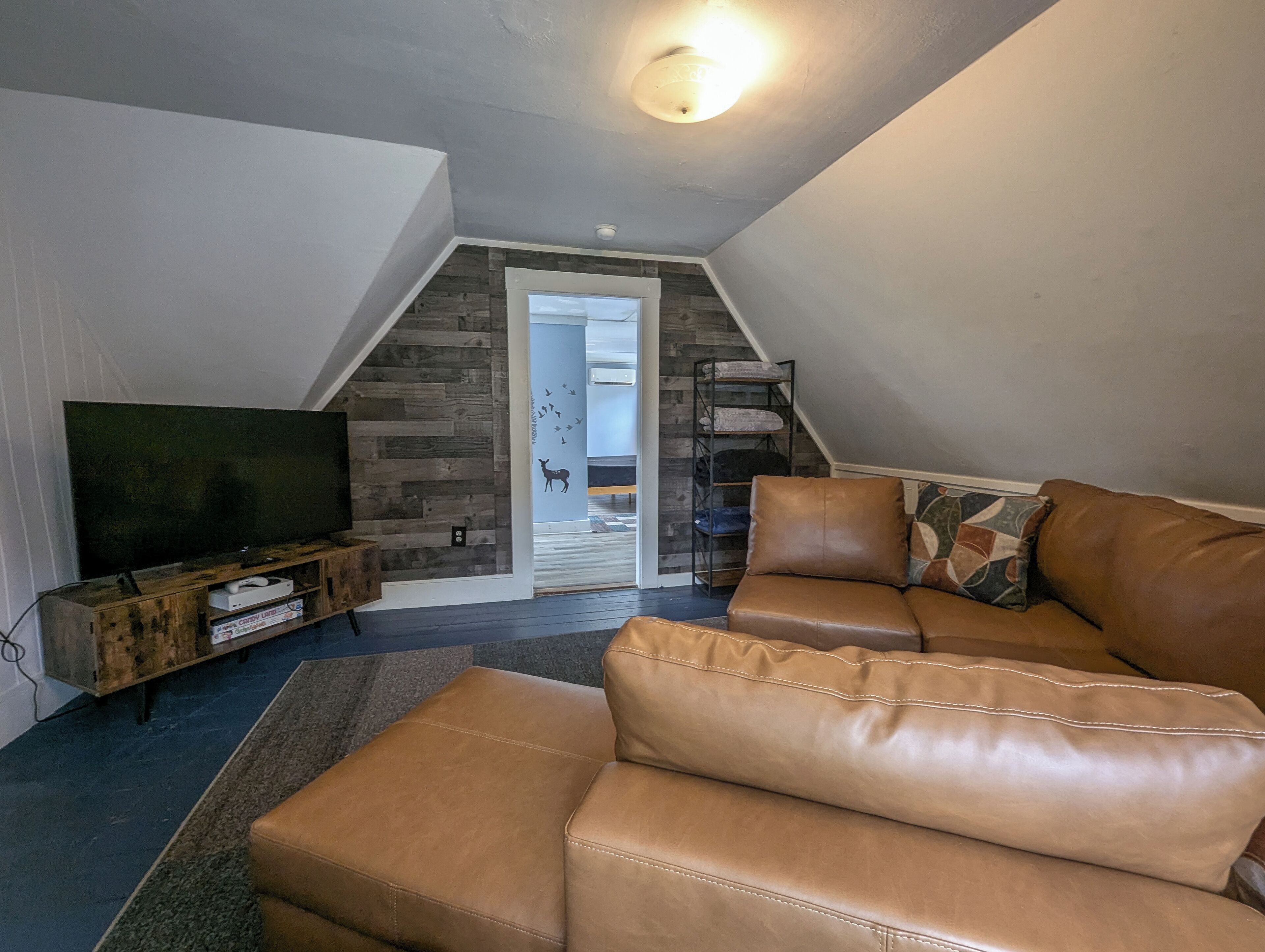 A cozy living room with a brown leather sofa, a flat-screen TV on a wooden stand, and a staircase leading to an upper level.