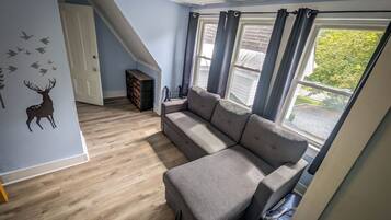 A room with a sectional sofa, a wooden floor, a wall decal of a deer, a staircase, and a window with curtains.