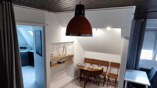 Ett modernt hotellrum med ett träpanelat tak, en matplats med bord och stolar, ett litet kök och en stor säng med en hoprullad handduk.