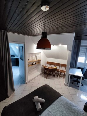 Ein modernes Hotelzimmer mit Holzboden, einem Essbereich mit Tisch und Stühlen, einer kleinen Küche und einem großen Bett mit gerolltem Handtuch.
