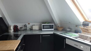 Ett modernt kök med en svart bänkskiva, en vit mikrovågsugn och en brödrost. Ett fönster sitter ovanför bänkskivan och släpper in naturligt ljus.