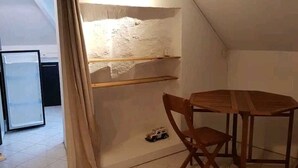Ett litet, svagt upplyst vindsrum med ett sluttande tak, ett träbord, en enda stol och en liten hylla.