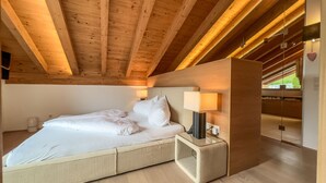 A modern bedroom with a wooden ceiling, a bed with white bedding, a bedside table with a lamp, and a view of a garden through a window. - Chalet Bergliebe - Zentral in Seefeld (Seefeld in Tirol)