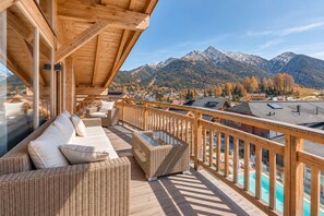 Une terrasse en bois, meublée de mobilier en osier, qui offre une vue sur un paysage montagneux et une piscine.