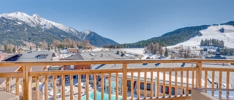 A wooden deck with a view of a snowy mountain range and a ski slope.