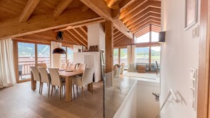 A spacious dining area with a wooden table and chairs, large windows offering a view of the outdoors, and a modern kitchen area with a hanging light fixture. - Chalet Bergliebe - Zentral in Seefeld (Seefeld in Tirol)