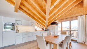 A modern kitchen with white cabinets, a wooden ceiling, and a dining area with a table and chairs. - Chalet Bergliebe - Zentral in Seefeld (Seefeld in Tirol)