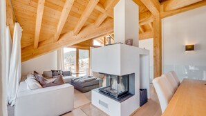 A modern living room with a fireplace, wooden beams, a sofa, and a dining table. - Chalet Bergliebe - Zentral in Seefeld (Seefeld in Tirol)