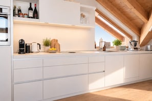 Une cuisine moderne avec des meubles blancs, une machine à café, une bouilloire et une bouteille de vin posée sur le comptoir.